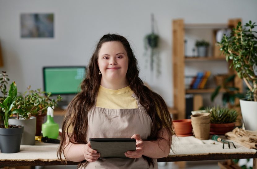 Mulher com síndrome de down sorri e segura um tablet.